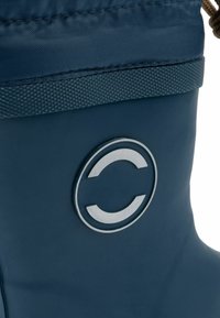 Botte imperméable navy avec tige texturée, bande en tissu contrastant et logo circulaire argenté. Elle est dotée d'un cordon de serrage en haut pour un ajustement réglable.
