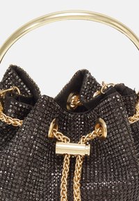 Sac en sequins noirs avec une poignée métallique dorée, des accents en chaîne et une fermeture ronde. La texture du tissu est lisse avec une finition brillante.