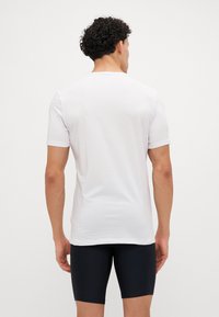 T-shirt blanc à manches courtes avec un col rond, texture lisse et coupe décontractée, associé à un short sombre, vu de l'arrière.