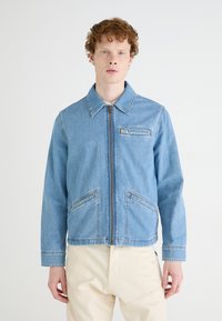 Jasnoniebieska kurtka dżinsowa z zamkiem błyskawicznym, kołnierzykiem i dwoma przednimi kieszeniami. Posiada kontrastujące szwy oraz metkę na kieszeni piersiowej.