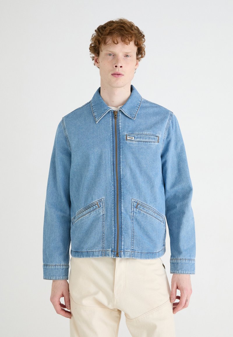 Jasnoniebieska kurtka dżinsowa z zamkiem błyskawicznym, kołnierzykiem i dwoma przednimi kieszeniami. Posiada kontrastujące szwy oraz metkę na kieszeni piersiowej.