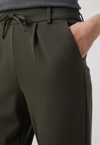 Olijfgroene, lichte broeken met een trekkoord in de taille, plooien aan de voorkant en zijzakken. Gladde textuur en getailleerde pasvorm.