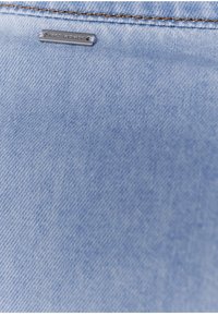 Light blue denim fabric with a smooth texture, featuring a small metal tag that reads "IKKS WOMEN," positioned near the top edge.