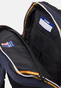 Zaino blu navy con una texture liscia, dotato di un compartimento con zip, accenti rossi, gialli e arancioni, e tasche interne per l'organizzazione.