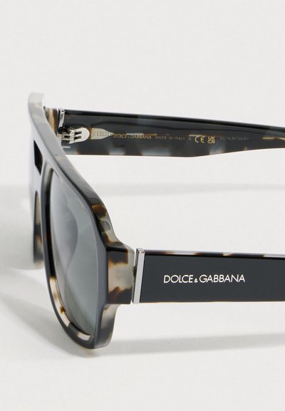Γυαλιά ηλίου Dolce & Gabbana με καφέ καβούκι χελώνας, τετράγωνα μαύρα φακούς και λογότυπο στο μπράτσο, φωτογραφημένα σε λευκό φόντο.