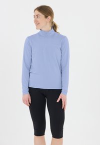 Vaaleansininen pitkähihainen urheilupaita, jossa on puolivetoketju kauluksessa. Yhdistetty mustiin capri-legginseihin. Pehmeä, joustava kangas ja istuva muotoilu.