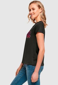 Black short-sleeve t-shirt featuring a bold, colorful graphic on the front. Soft fabric with a relaxed fit, paired with light blue jeans.