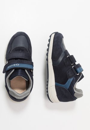 Baskets bleu marine avec une texture en daim et en cuir, double bande Velcro, semelle en caoutchouc, et des accents gris et bleus sur le côté.