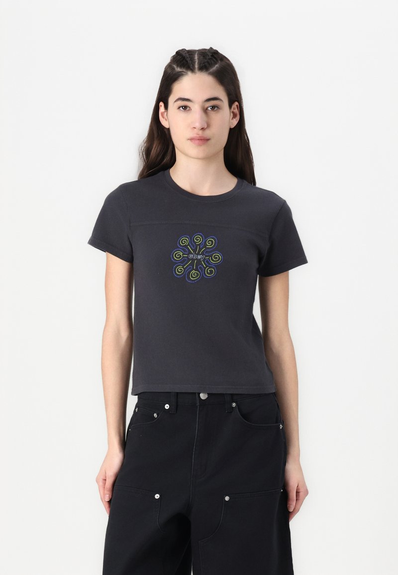 T-shirt nera in cotone con maniche corte, caratterizzata da un ricamo a spirale colorato al centro, abbinata a pantaloni neri a vita alta.
