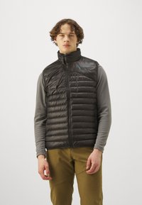 Sorte puffer vest med høj krave, vandret quiltning og lynlås foran. Accentueret med et lille blåt logo på venstre skulder.
