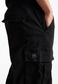 Zwarte cargobroek van duurzaam materiaal, met een zijzak en een vierkante Pull&Bear logo patch en een strak, eenvoudig ontwerp.