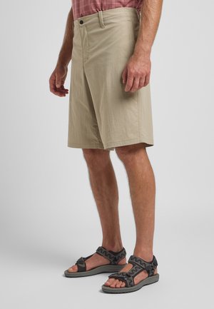 Beige shorts with a relaxed fit, made of lightweight fabric. Features a front pocket and a button closure. Paired with black strappy sandals.