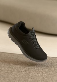 Melnas sporta kurpes ar acs materiālu, saistītu dizainu un pelēku zoli. Sānos atrodas logo, kā arī teksturēta virsma labākai saķerei.