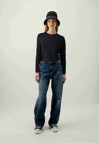 Μαύρη μακρυμάνικη μπλούζα, κατεστραμμένα μπλε τζιν και μαύρο καπέλο bucket με ρίγες. Μαύρα αθλητικά παπούτσια ολοκληρώνουν την καθημερινή εμφάνιση.