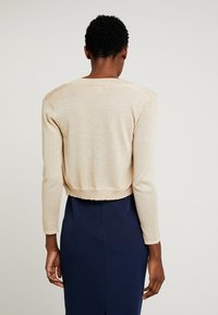 Zkrácený svetr s dlouhým rukávem v metalické béžové barvě, s kulatým výstřihem a vroubkovaným lemem, doplněný námořnickou sukní.