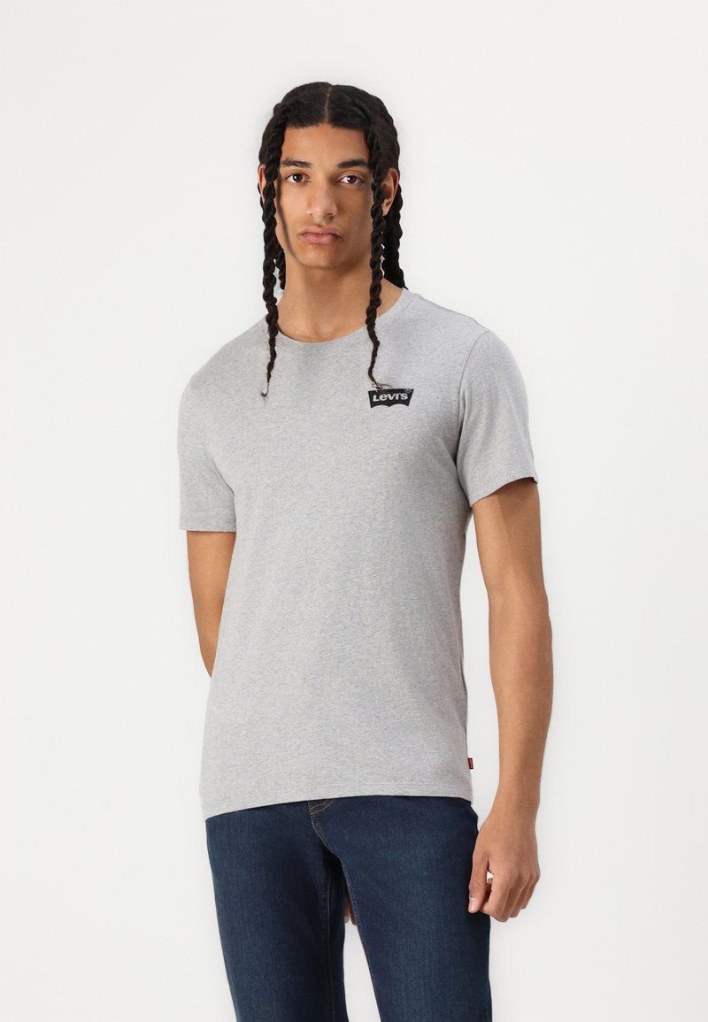 Camiseta de algodón gris con mangas cortas, cuello redondo y un pequeño logo negro de Levi's en el pecho. Con jeans de color azul oscuro.