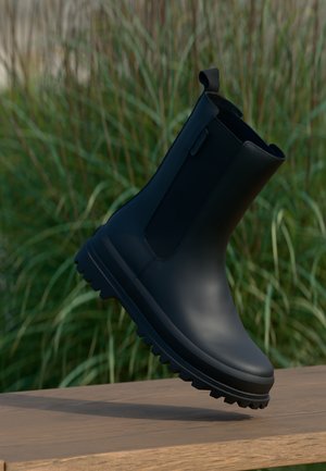 Bota de tobillo de goma negra con un acabado texturizado, puntera redondeada y una suela pronunciada y resistente. Cuenta con un tirador para facilitar su uso.