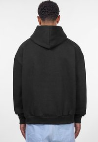 Sweat à capuche noir avec une coupe loose, des poignets et un ourlet côtelés, et un design à couture plate. Le tissu semble doux et légèrement texturé.