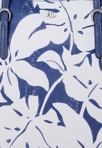 Vit tygväska med ett blått blommönster, silverdetaljer och blå texturerade remmar.