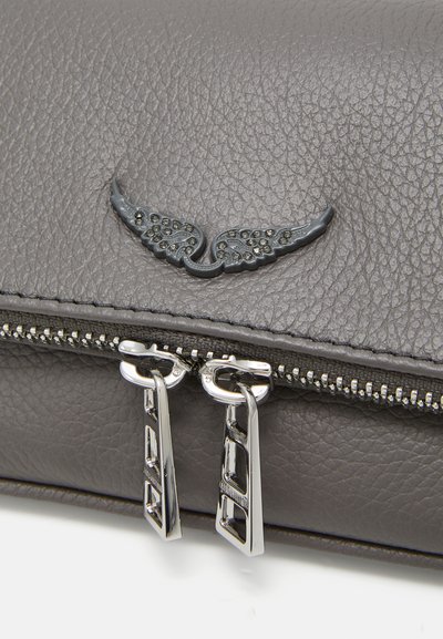 Pochette en cuir gris présentant une finition texturée, un emblème décoratif en forme d'aile et des fermetures éclair en métal argenté avec des tirettes distinctives.
