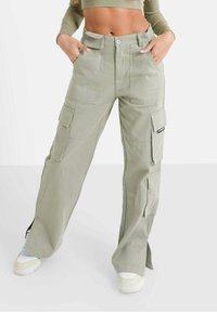 Pantalons cargo vert clair avec une coupe ample, dotés de plusieurs poches, d'une fermeture à bouton à l'avant et de zips sur les poignets.