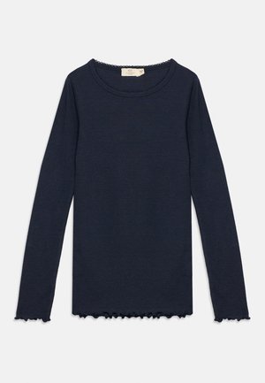 Granatowy, długi sweter z okrągłym dekoltem i falistymi krawędziami na mankietach i dole, ułożony płasko na białym tle.