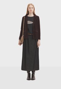 Blazer in corduroy marrone, camicia nera con dettagli a fantasia, gonna maxi in denim scuro e stivaletti alla caviglia in pelle marrone. Inclusa borsa a spalla.