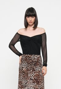 Haut noir décolleté avec un détail avant torsadé et des manches longues transparentes, associé à une jupe fluide à imprimé léopard dans des tons terreux.