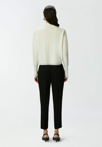 Kremasti pleteni džemper s kratkim rubom, rebrastim manžetama, uparen s krojenim crnim hlačama. Pogled sa stražnje strane, glatka tekstura i ravna silueta.