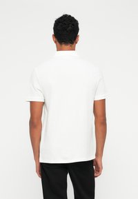 Camisa polo branca com colarinho clássico e mangas curtas, feita de algodão. Design simples, sem padrões ou detalhes visíveis.