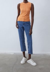 Orange ruggad ärmlös topp med en fram-söm, kombinerad med blå raka jeans och vita sneakers med en kontrasterande häldetalj.