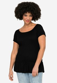 Černý peplum top vyrobený z texturované tkaniny, s krátkými rukávy a širokým výstřihem, s volánovým lemem. V kombinaci se světlemodrými džíny.