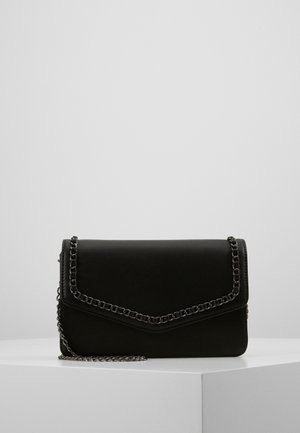 Borsa nera in finta pelle con tracolla a catena, caratterizzata da un design a busta e un particolare bordino cucito, posata su una superficie bianca.