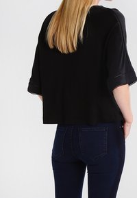 Svart kort topp med lösa ärmar, med rund halsringning och synliga sömdetaljer. Matchad med mörkblå åtsittande jeans.