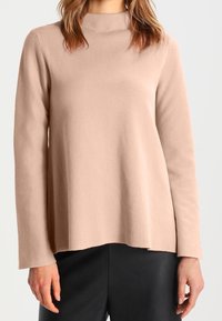 Ljusrosa långärmad topp med hög halsringning, tillverkad av mjukt tyg; har en avslappnad passform och en något rundad nederkant.