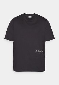 Musta lyhythihainen Calvin Klein -t-paita, jossa on pyöreä pääntie ja valkoinen logo teksti etuosan alaosassa.