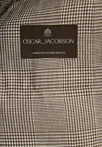 Brown and white houndstooth-patterned fabric with a textured finish; features an Oscar Jacobson brand label stating "Swedish Craftsmanship Since 1903."