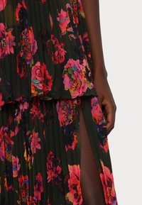 Jupe plissée foncée avec motif floral rose vif et rouge et fente jusqu'à la cuisse, montrée avec une main visible reposant sur le côté.