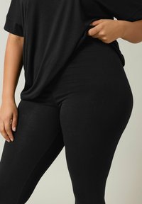 Zwarte leggings gemaakt van zachte, rekbare stof, met een gladde textuur en een getailleerde pasvorm. Draagt bij een losse zwarte top.