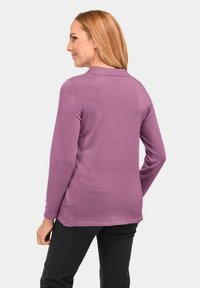 Paarse langekatoen polo met een kraag, geribbelde textuur en zijsplitten. Draag met donkere broek, met een relaxte pasvorm en een achteraanzicht.