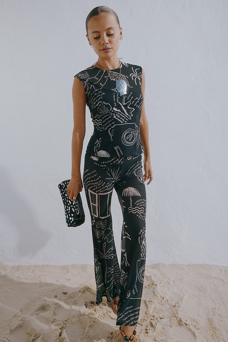 Completino nero con grafiche astratte bianche, corsetto attillato, pantaloni a zampa e design senza maniche; abbinato a una pochette decorata.