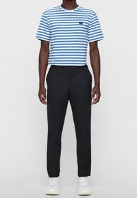 Modro-bílý pruhovaný tričko s krátkým rukávem a malým logem na hrudi, v kombinaci s černými zúženými kalhotami a bílými teniskami.