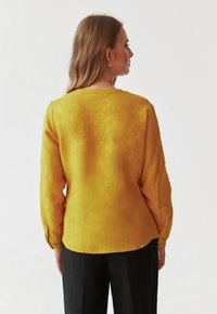 Mosterdgele blouse met lange mouwen en een gebogen zoom in een relaxte fit. Kenmerkt zich door een soepele textuur en een eenvoudige ronde halslijn aan de achterkant.