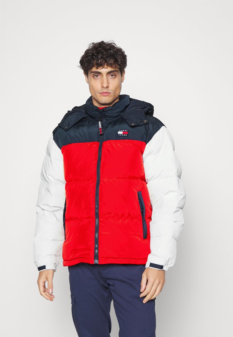 Chaqueta acolchada con torso rojo, hombros marino y mangas blancas. Cuenta con cierre de cremallera, capucha y parche con logo en el pecho.