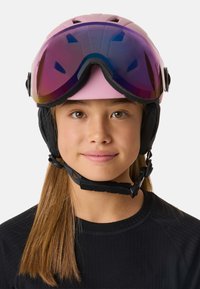 Roze skihelm met geïntegreerde zwarte oorstukken en paarsgetinte skibril. Heeft een slank ontwerp en een verstelbare kinband.