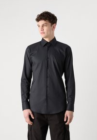 Camisa negra de manga larga con cuello, con un frente abotonado, textura suave y diseño ajustado. Sin patrones ni acentos visibles.