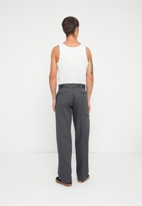 Grå bukser med en afslappet pasform, lavet af stof, med en flad talje, baglommer og sidelommer. Båret med en hvid tanktop.