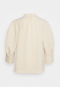 Blusa color crema con scollatura rotonda, maniche a sbuffo e dettagli arricciati sul retro e sulle cuciture delle spalle. Tessuto con finitura liscia.