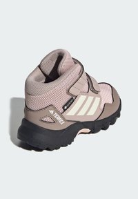 Zapato de senderismo rosa y gris con tejido de malla, correa de velcro y suela de goma negra. Cuenta con tres franjas blancas y una etiqueta Gore-Tex.