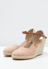 Wedge espadrilles with a soft pink suede upper, brown ankle strap, and woven jute sole. Round toe and textured side detailing.